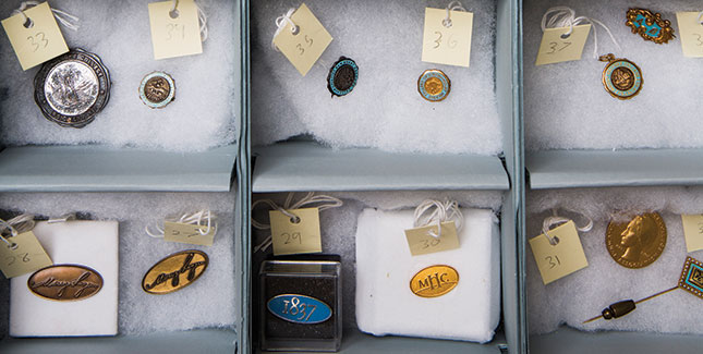 An archival storage box holds the Archives’ jewelry and pin collection, including class rings, charms, and other symbolic items.