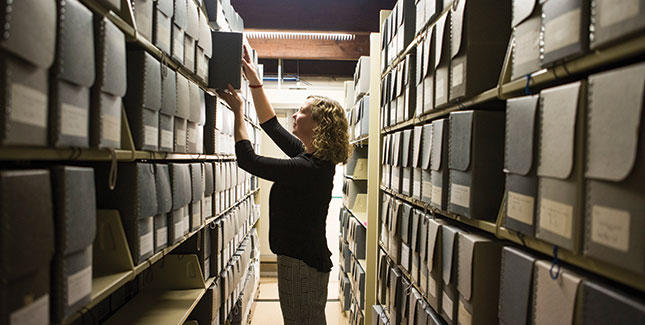 Head of Archives and Special Collections Leslie Fields in the Archives stacks surrounded by boxes of College history.