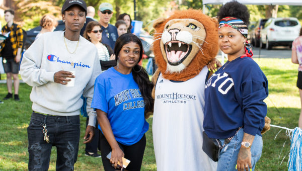 A student and family poses with Paws, the lion mascot, by the Orientation welcome tent.